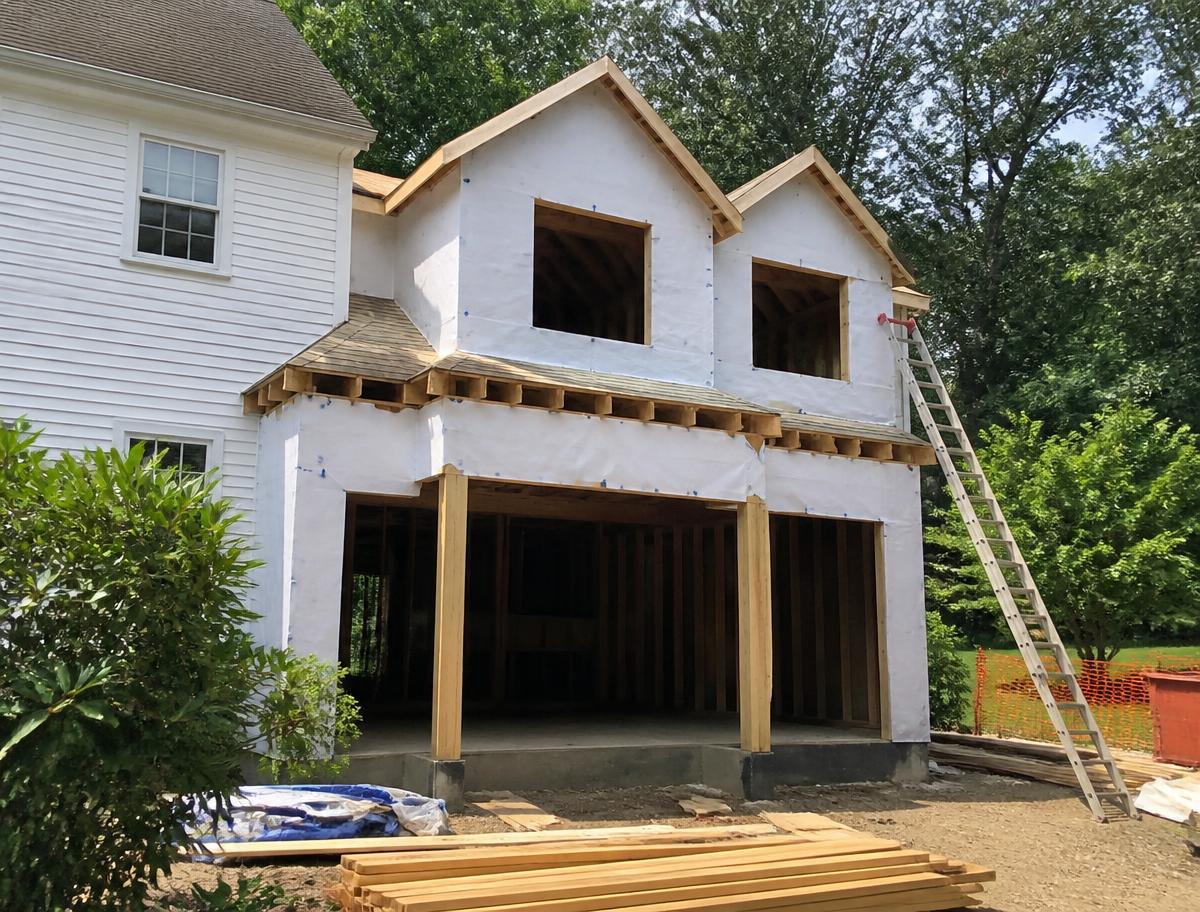 Two story home addition under construction attached to an existing colonial house